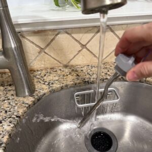 "An anti-calc rod being rinsed under a running faucet."